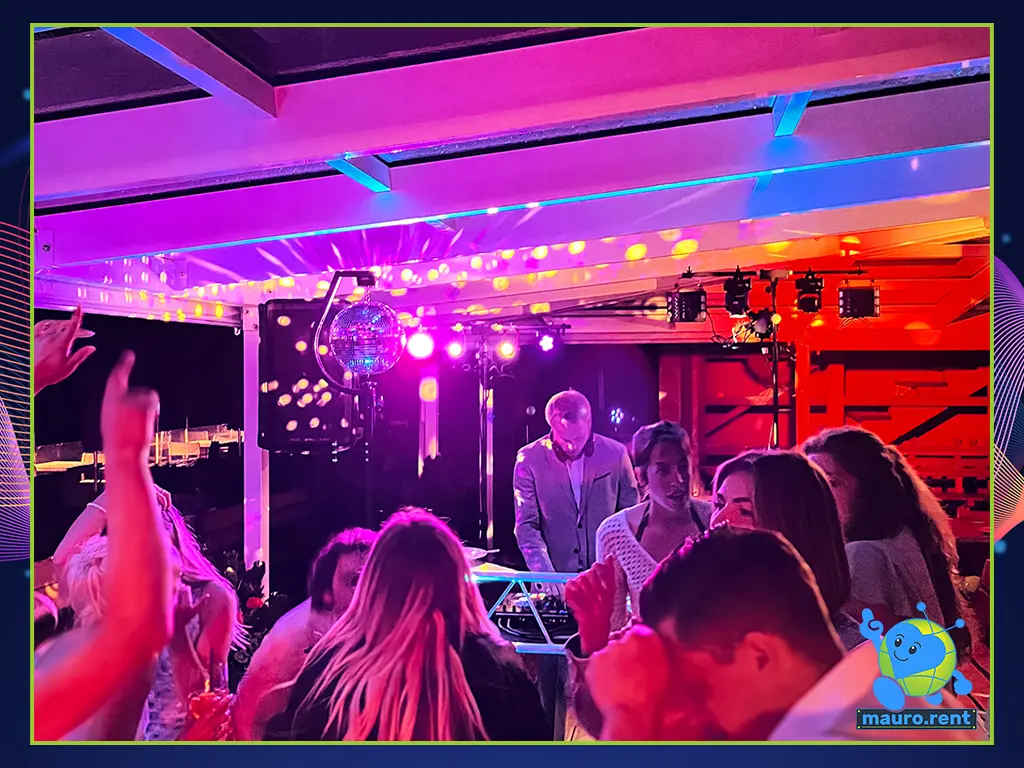 High-energy wedding dance floor full of swing inside the Col Pradat lodge with DJ Willionaire mixing in the background under professional party lighting.