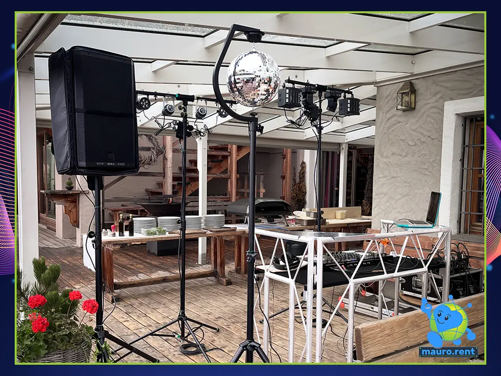 Detailed view of the mauro.rent DJ booth and lighting setup featuring RCF Art 915-A, Accu Stand table, Flyht Pro rack, Furman power conditioner, and BeamZ lighting fixtures.