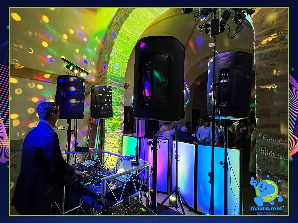Technical wide shot from Mauro's control rack looking toward DJ Niclas performing inside the historic stone-arch dance floor at Abbazia San Faustino.